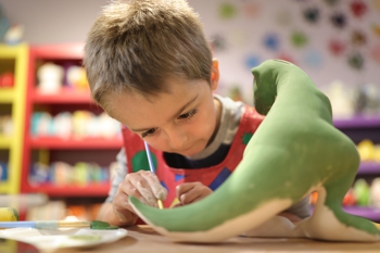 Boy painting ceramic dinosaur model